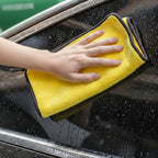 Hand using a yellow microfiber cloth to clean a car window with red text overlay.