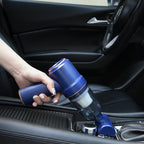 Hand holding a blue handheld vacuum cleaner inside a car.